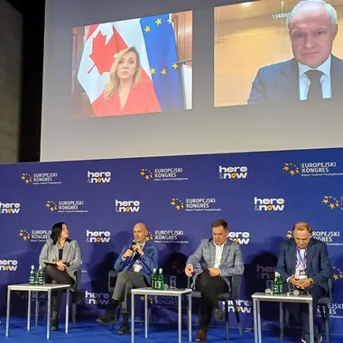 A panel discussion on stage at a European business congress, the speakers carried on a screen above